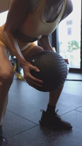 A close-up, 9:16 vertical video frame capturing an athlete in the middle of a dynamic movement using a textured medicine ball in a gym setting.